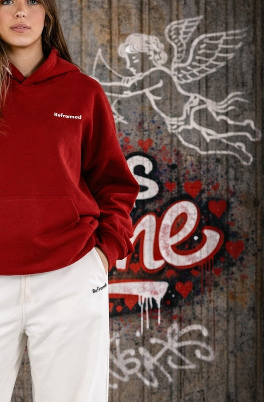Person wearing a red hoodie with text, standing in front of a decorative wall with hearts and graffiti.